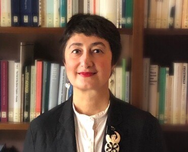 A person with short dark hair wearing a black blazer and light shirt.