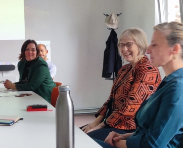 A group of four people sit at a conference table, engaged and smiling. 