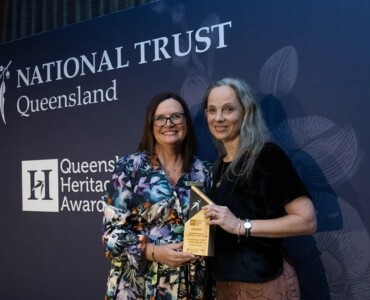 Two women pose together holding an award in front of a backdrop that reads 